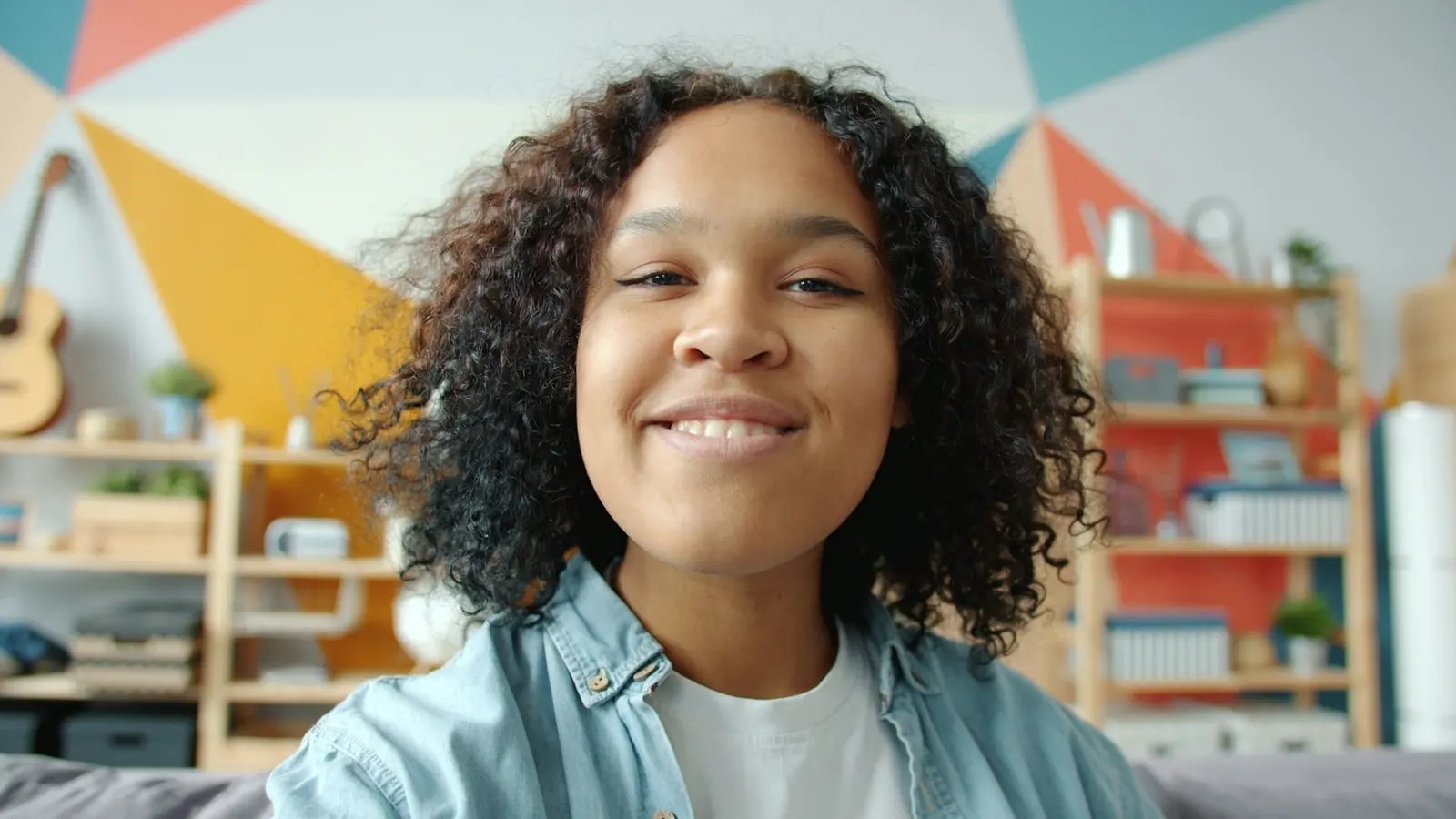 A smiling girl talking to the screen in a bright, colourful room