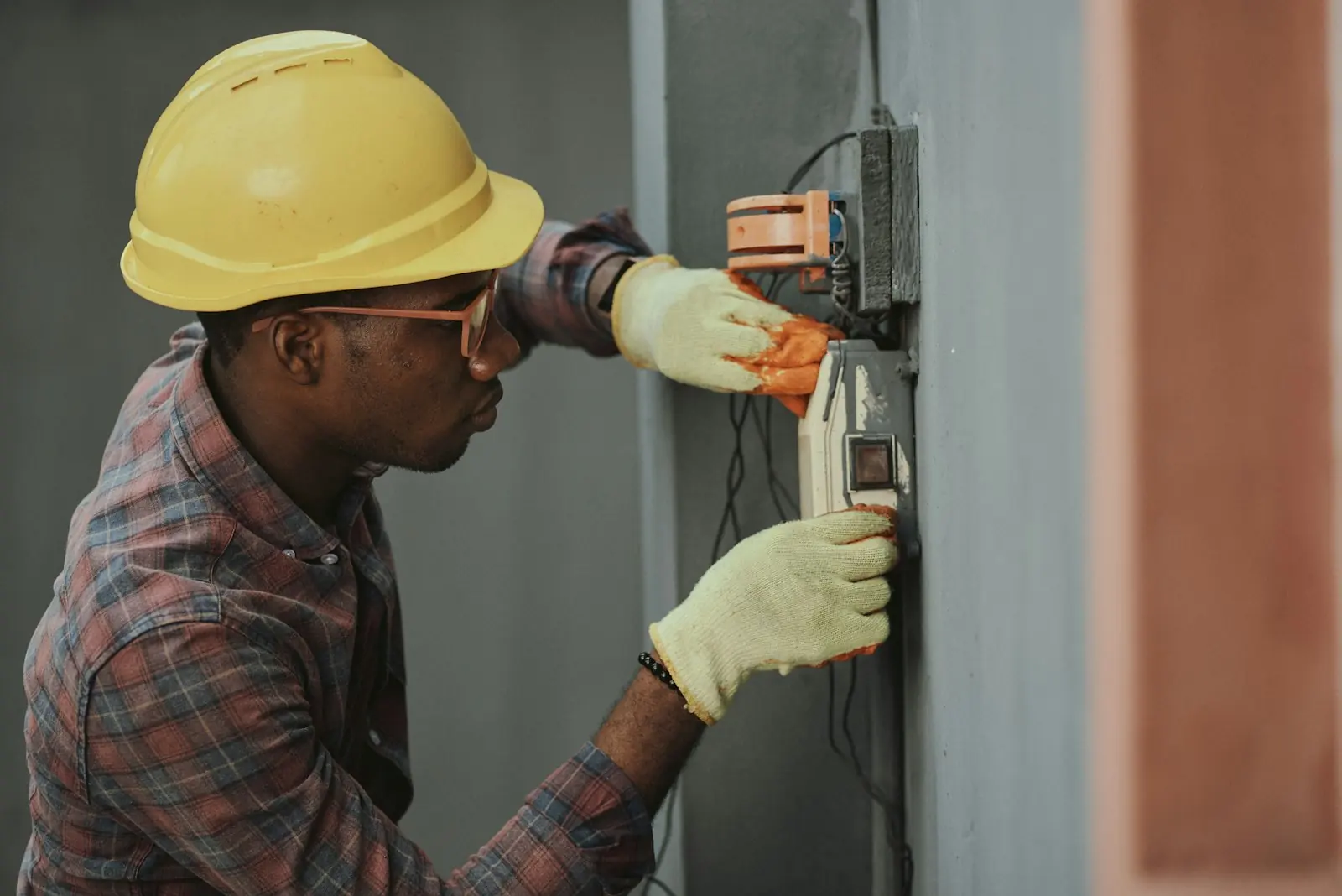 An electrician in a yellow hard hat wiring a unit on a wall