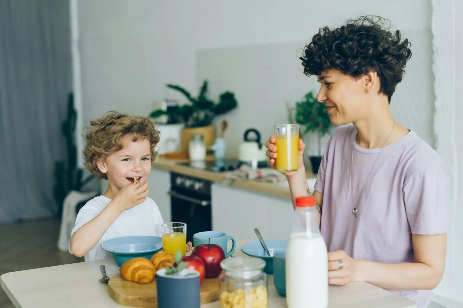 A mum and her young son at breakfast in a bright kitchen, a bottle of milk on the table