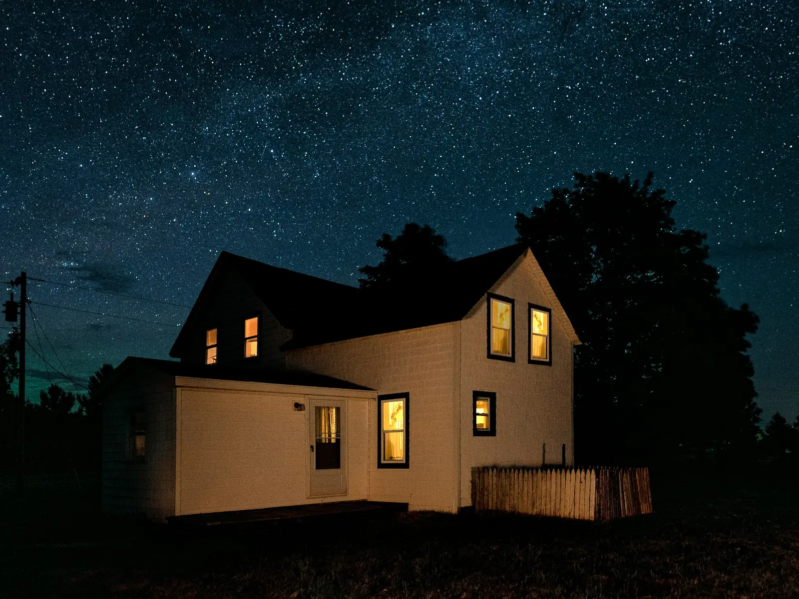 A house at night under the stars, lights on inside