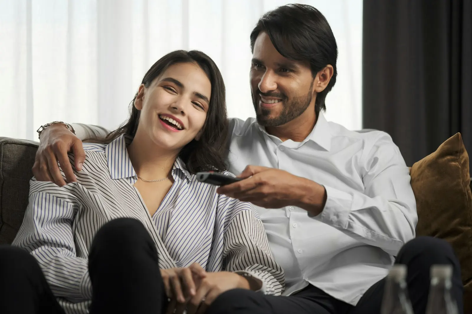 A couple laughing on the sofa, one of them holding the TV remote